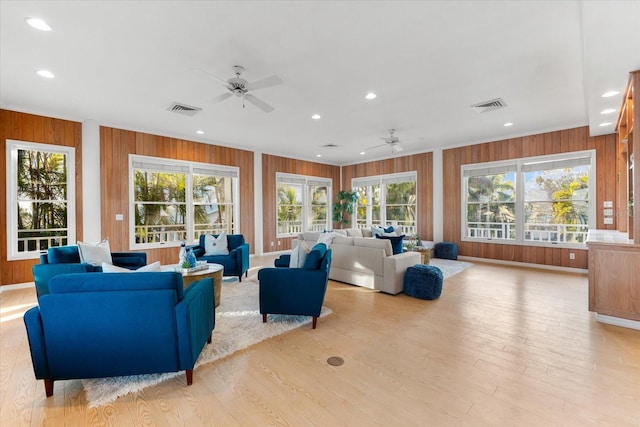 living room featuring ornamental molding, light hardwood / wood-style floors, ceiling fan, and wood walls