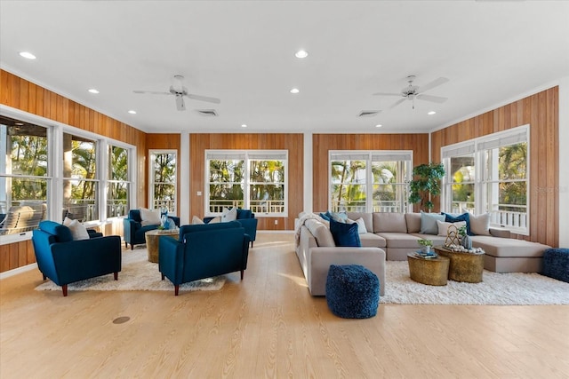 living area with a ceiling fan, wood finished floors, visible vents, wood walls, and crown molding