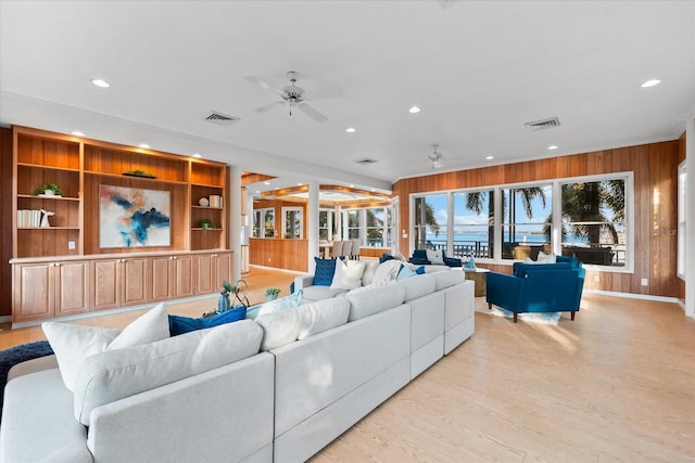 living room with light hardwood / wood-style flooring, built in features, ceiling fan, and wood walls