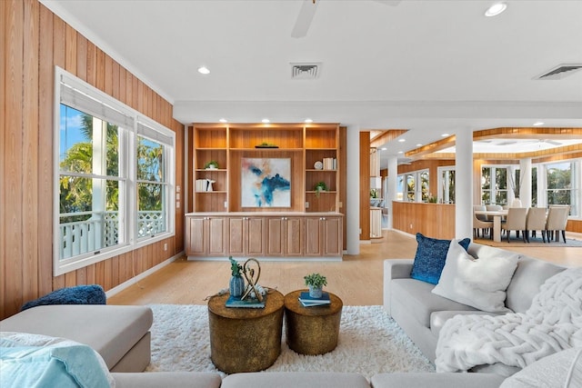 living room with built in shelves, ornamental molding, light wood-type flooring, and wood walls