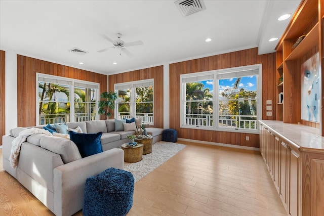 living room featuring ornamental molding, ceiling fan, light hardwood / wood-style floors, and wood walls