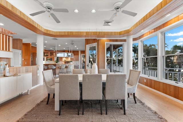 dining room featuring ceiling fan, light hardwood / wood-style floors, and wood walls