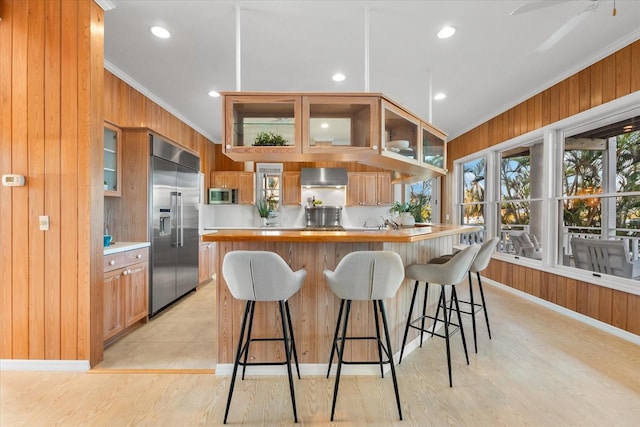 kitchen featuring ornamental molding, appliances with stainless steel finishes, wood walls, and wall chimney range hood