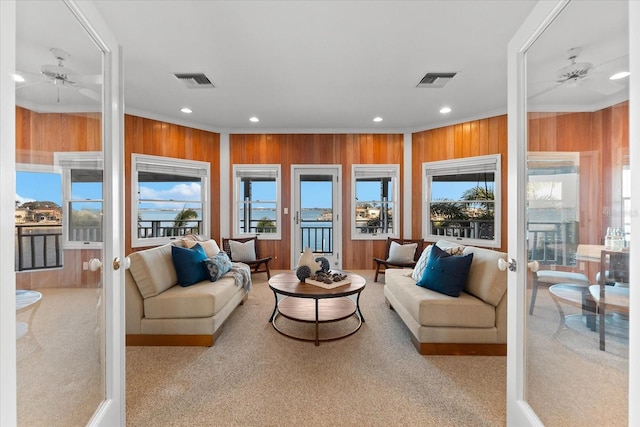 living room with ceiling fan, ornamental molding, light colored carpet, and wood walls