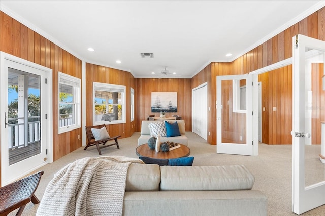 living room featuring french doors, ornamental molding, light carpet, and wood walls