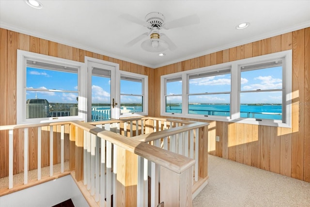 interior space with crown molding, a water view, light carpet, and wooden walls