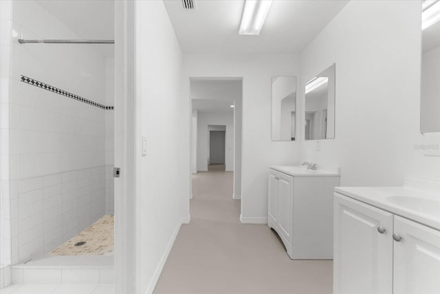 full bath with two vanities, baseboards, a tile shower, and a sink