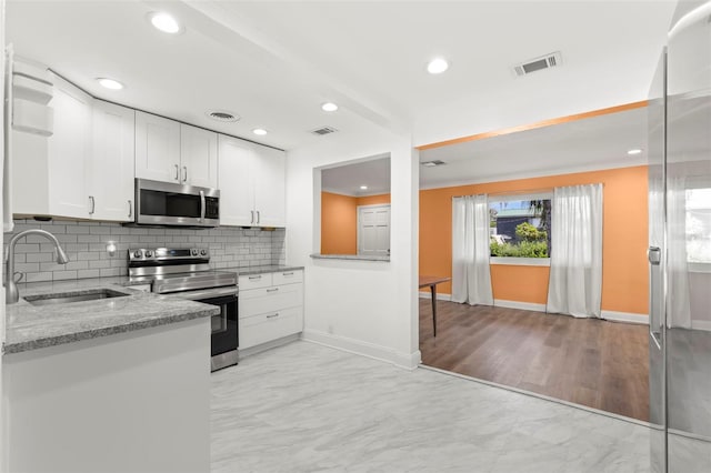 kitchen featuring white cabinets, appliances with stainless steel finishes, tasteful backsplash, sink, and light stone counters