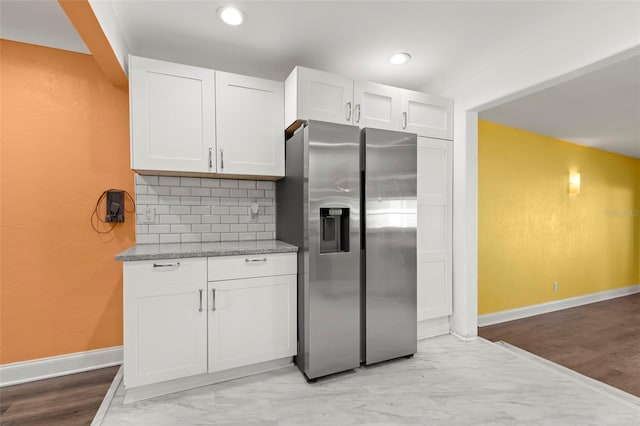 kitchen featuring stainless steel refrigerator with ice dispenser, white cabinetry, decorative backsplash, and light stone countertops