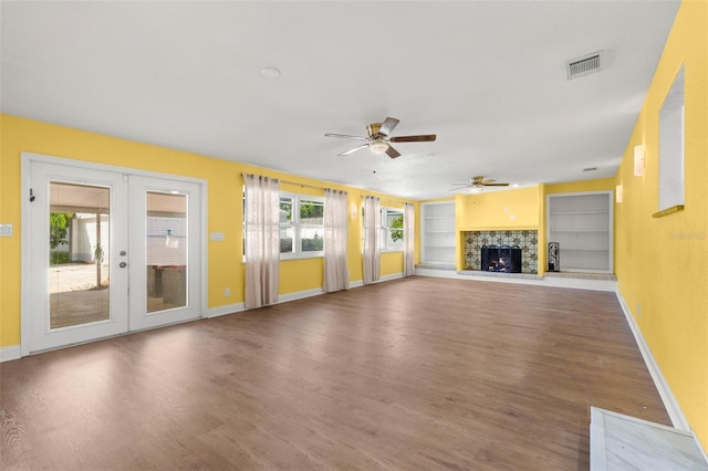 unfurnished living room with hardwood / wood-style flooring, ceiling fan, a fireplace, built in features, and french doors