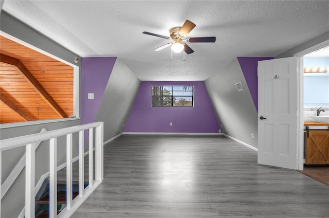 additional living space featuring wood-type flooring, ceiling fan, a textured ceiling, lofted ceiling, and sink