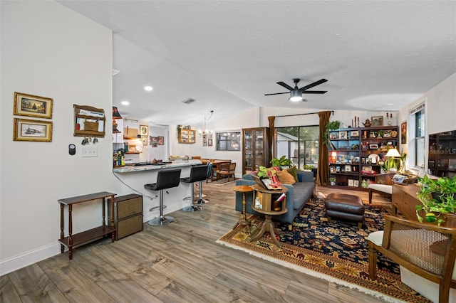 living room featuring a textured ceiling, ceiling fan with notable chandelier, hardwood / wood-style flooring, and lofted ceiling