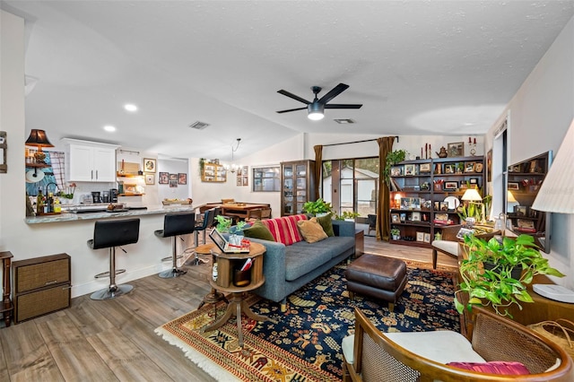 living room featuring ceiling fan with notable chandelier, vaulted ceiling, a textured ceiling, and light hardwood / wood-style flooring