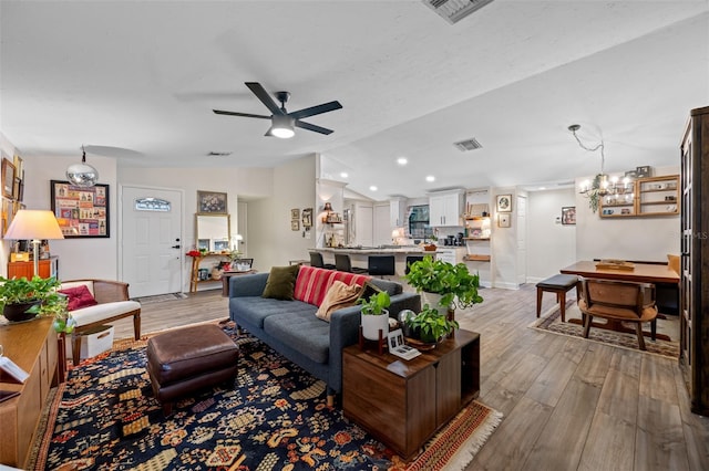 living room featuring ceiling fan with notable chandelier, vaulted ceiling, and light hardwood / wood-style flooring