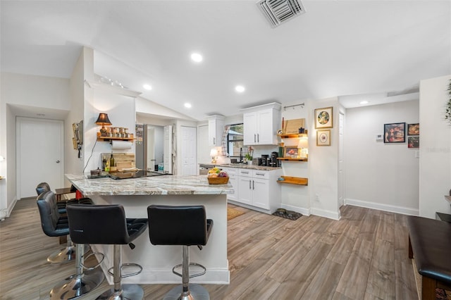 kitchen featuring white cabinetry, light stone countertops, a kitchen breakfast bar, light hardwood / wood-style floors, and black electric stovetop