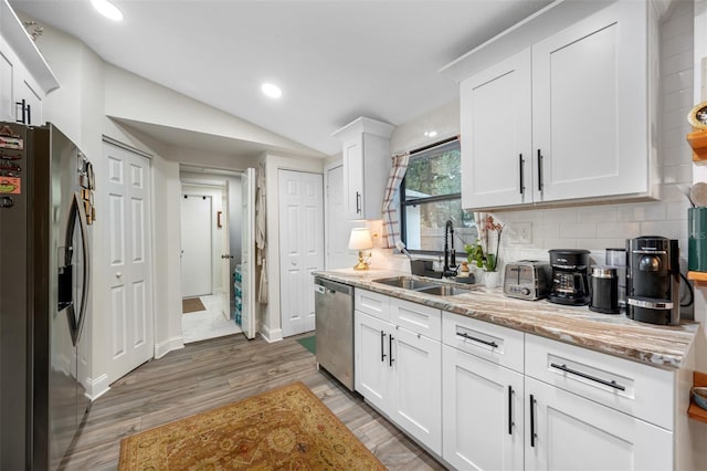 kitchen featuring sink, stainless steel appliances, light stone counters, lofted ceiling, and white cabinets