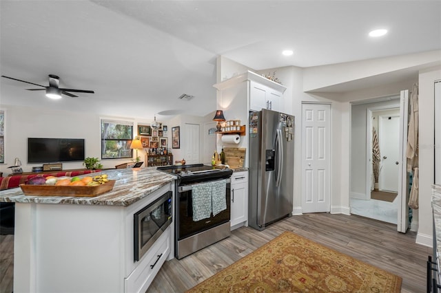 kitchen with hardwood / wood-style flooring, ceiling fan, appliances with stainless steel finishes, light stone counters, and white cabinetry