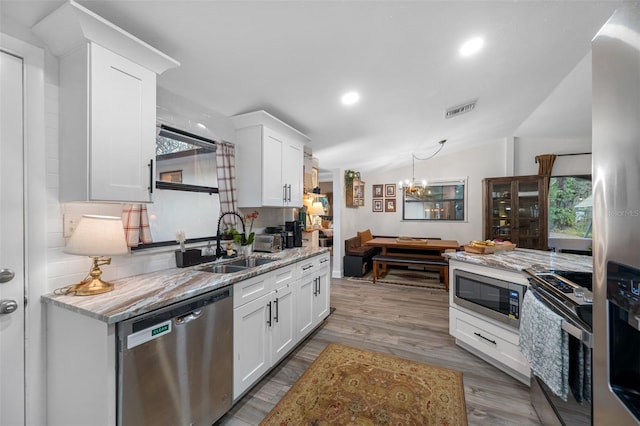 kitchen with light stone countertops, white cabinetry, stainless steel appliances, and vaulted ceiling