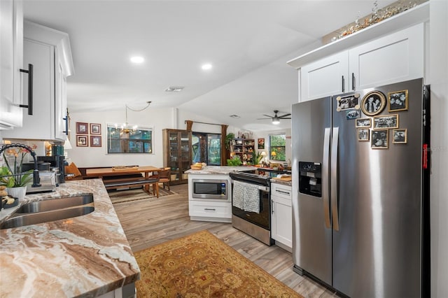 kitchen featuring kitchen peninsula, light stone countertops, ceiling fan with notable chandelier, stainless steel appliances, and white cabinetry