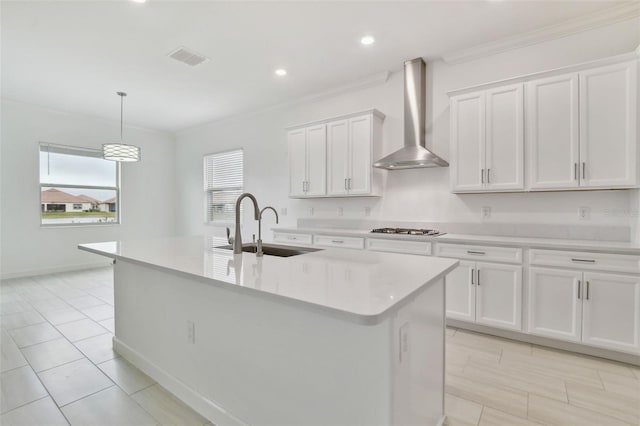 kitchen featuring stainless steel gas stovetop, white cabinets, hanging light fixtures, a kitchen island with sink, and wall chimney range hood