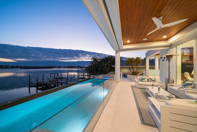 pool at dusk with a patio area, ceiling fan, a water and mountain view, and a boat dock