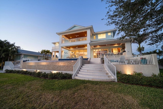 back house at dusk featuring a balcony and a yard