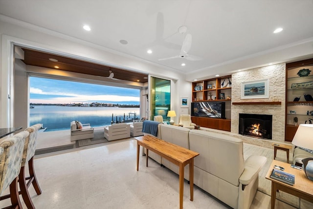 living room featuring a stone fireplace, ceiling fan, built in features, and crown molding