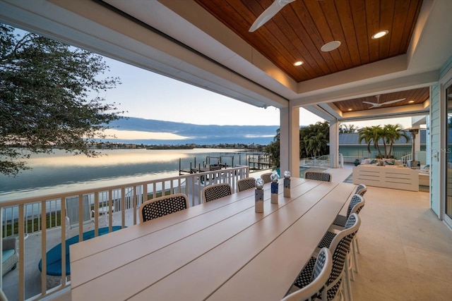 patio terrace at dusk featuring a water view and ceiling fan