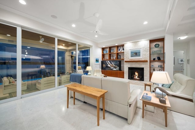 living room featuring built in shelves, a stone fireplace, ceiling fan, and ornamental molding