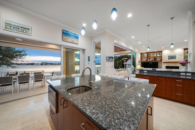 kitchen with a large island with sink, dark stone counters, sink, hanging light fixtures, and a fireplace