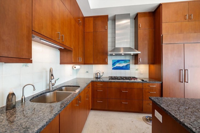 kitchen with sink, stainless steel gas cooktop, dark stone countertops, and wall chimney range hood