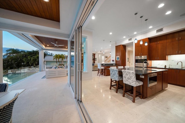 kitchen with stainless steel oven, a spacious island, sink, hanging light fixtures, and a breakfast bar area