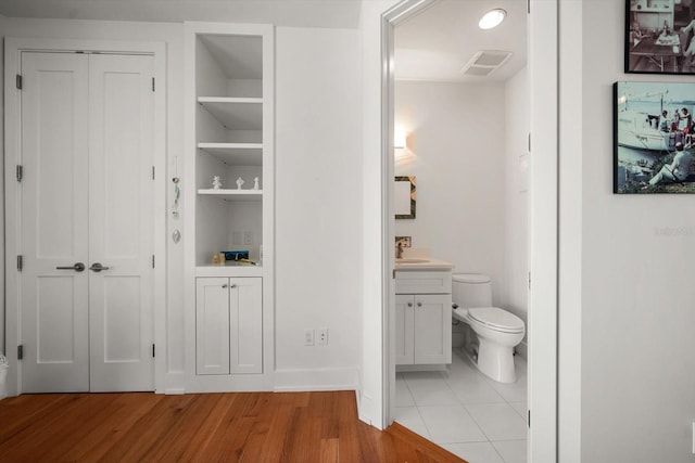 bathroom featuring built in shelves, vanity, toilet, and hardwood / wood-style floors