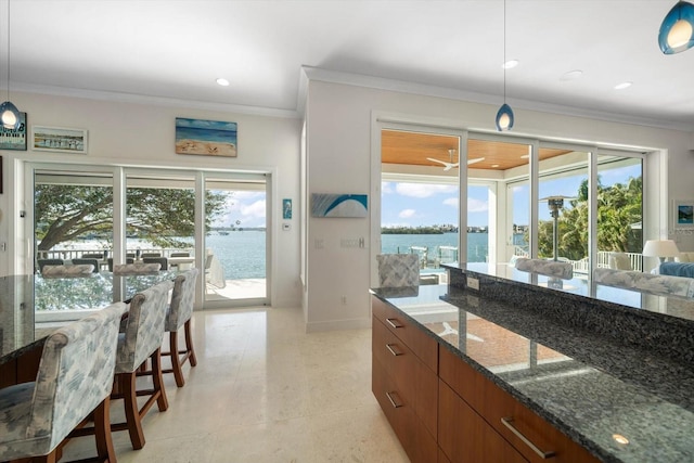 kitchen featuring dark stone counters, a water view, ornamental molding, decorative light fixtures, and a breakfast bar area