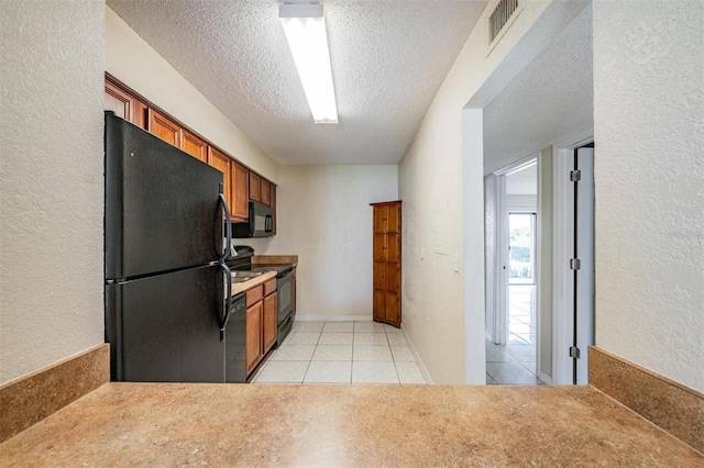 kitchen with black appliances, light tile patterned floors, and a textured ceiling