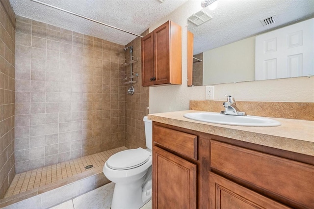 bathroom featuring tile patterned flooring, a textured ceiling, tiled shower, toilet, and vanity