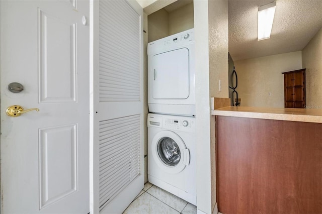 washroom with a textured ceiling, light tile patterned floors, and stacked washer and clothes dryer