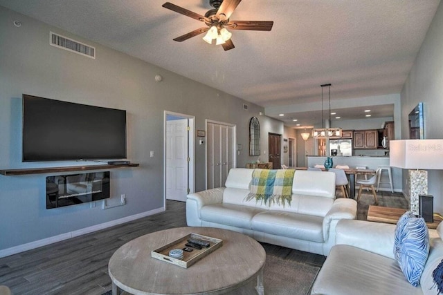 living room with ceiling fan, a textured ceiling, and dark hardwood / wood-style floors