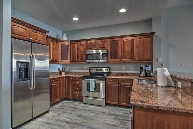 kitchen featuring a textured ceiling, stainless steel appliances, dark stone countertops, sink, and light hardwood / wood-style flooring