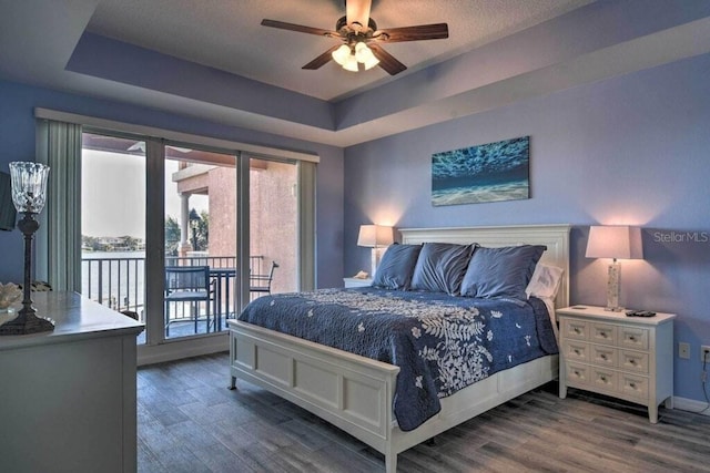 bedroom featuring ceiling fan, dark hardwood / wood-style flooring, access to outside, and a tray ceiling