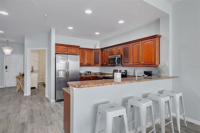 530 S Gulfview Blvd Unit 205, Clearwater, FL 33767 - kitchen featuring stainless steel appliances, a peninsula, light wood-type flooring, light stone counters, and a textured ceiling
