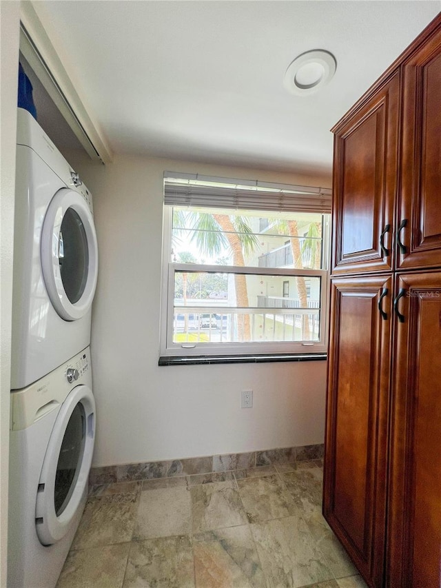 laundry area featuring stacked washer and clothes dryer and cabinets