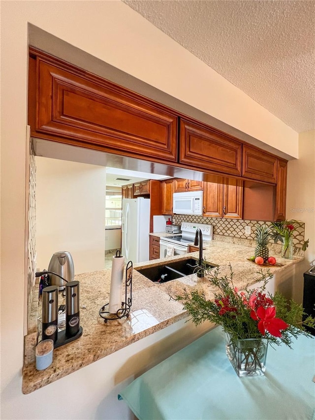 kitchen with white appliances, light stone countertops, a textured ceiling, kitchen peninsula, and backsplash