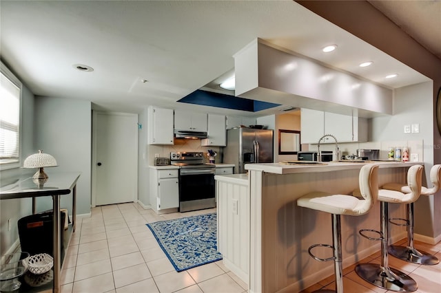 kitchen featuring kitchen peninsula, light tile patterned floors, tasteful backsplash, white cabinetry, and appliances with stainless steel finishes