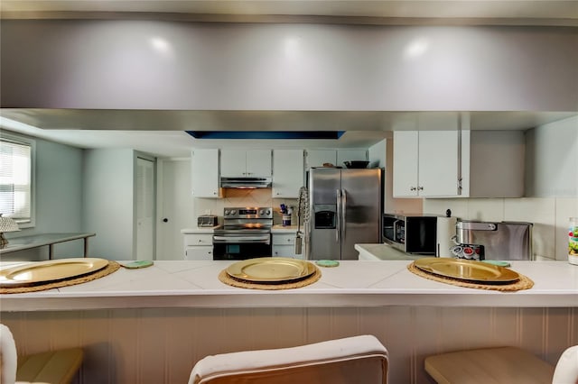 kitchen featuring stainless steel appliances, kitchen peninsula, a breakfast bar, white cabinetry, and tasteful backsplash