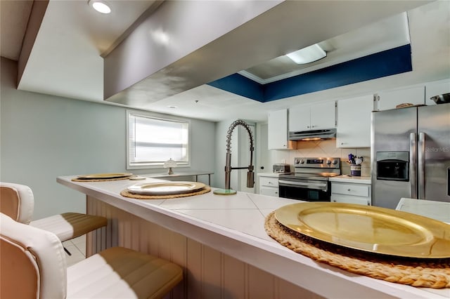 kitchen featuring stainless steel appliances, white cabinets, a kitchen breakfast bar, and backsplash