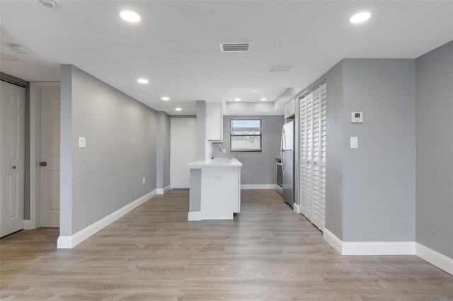 kitchen featuring white cabinets, light hardwood / wood-style floors, sink, stainless steel fridge, and kitchen peninsula