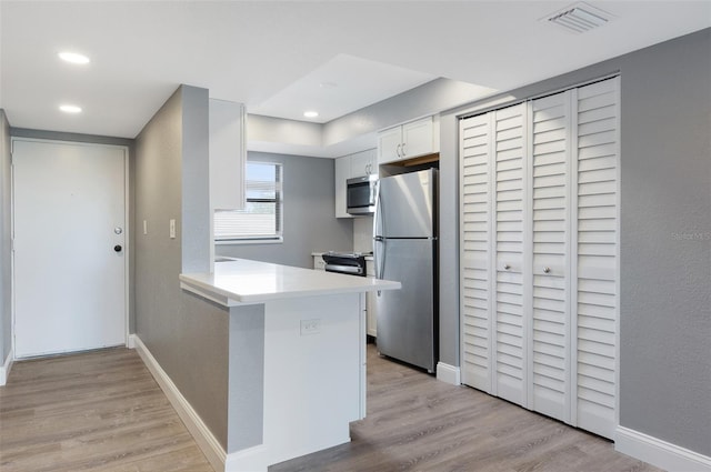 kitchen with white cabinets, appliances with stainless steel finishes, kitchen peninsula, and light wood-type flooring