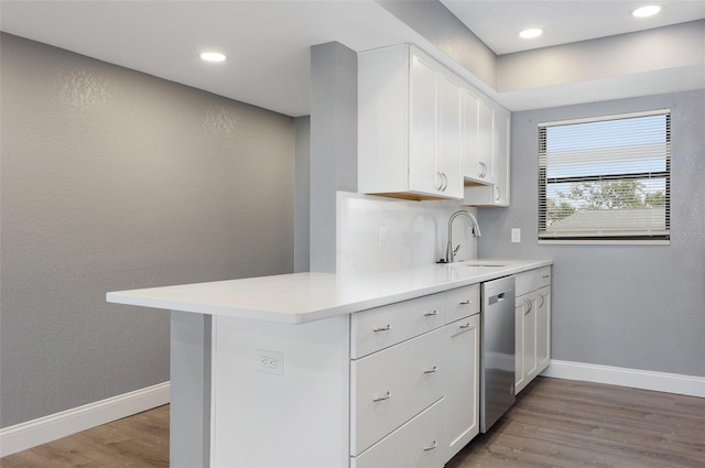 kitchen with white cabinetry, sink, kitchen peninsula, hardwood / wood-style flooring, and stainless steel dishwasher