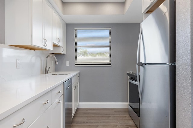 kitchen with white cabinets, appliances with stainless steel finishes, tasteful backsplash, sink, and light wood-type flooring